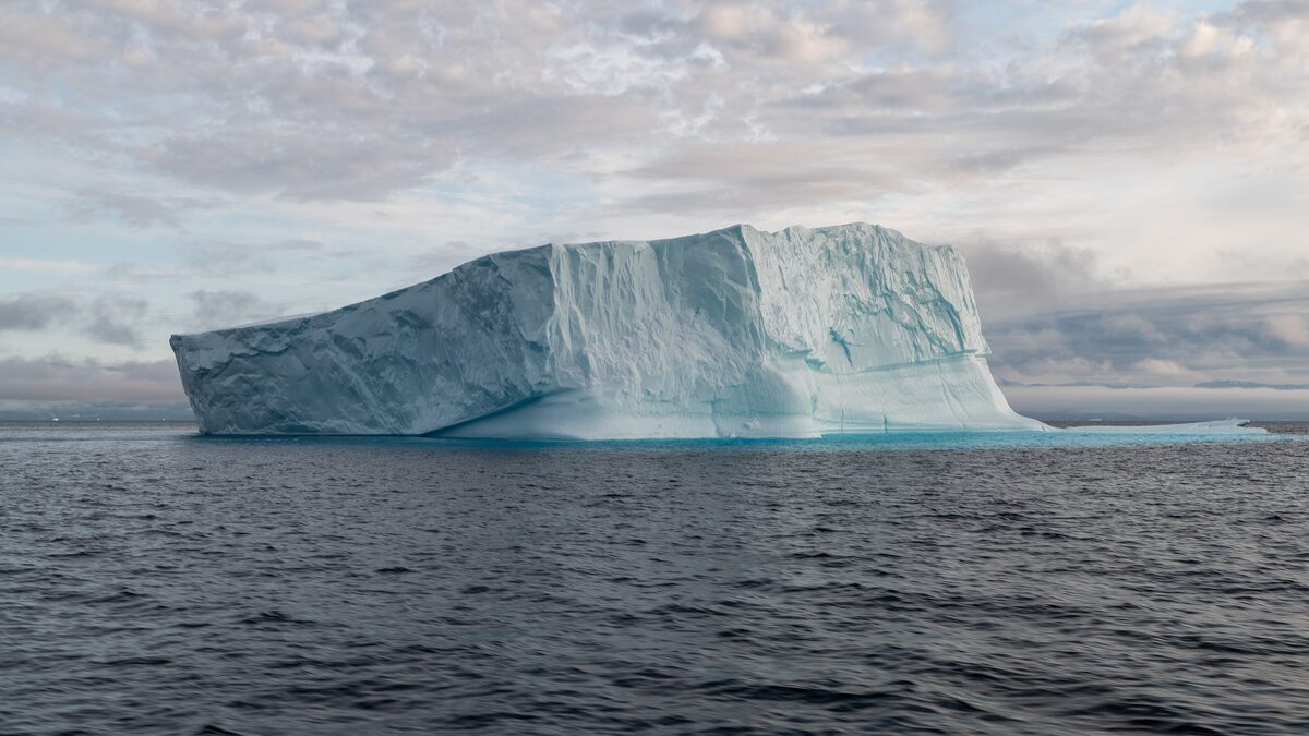 A large iceberg floating in Disko Bay under a pale sky, seen from the water