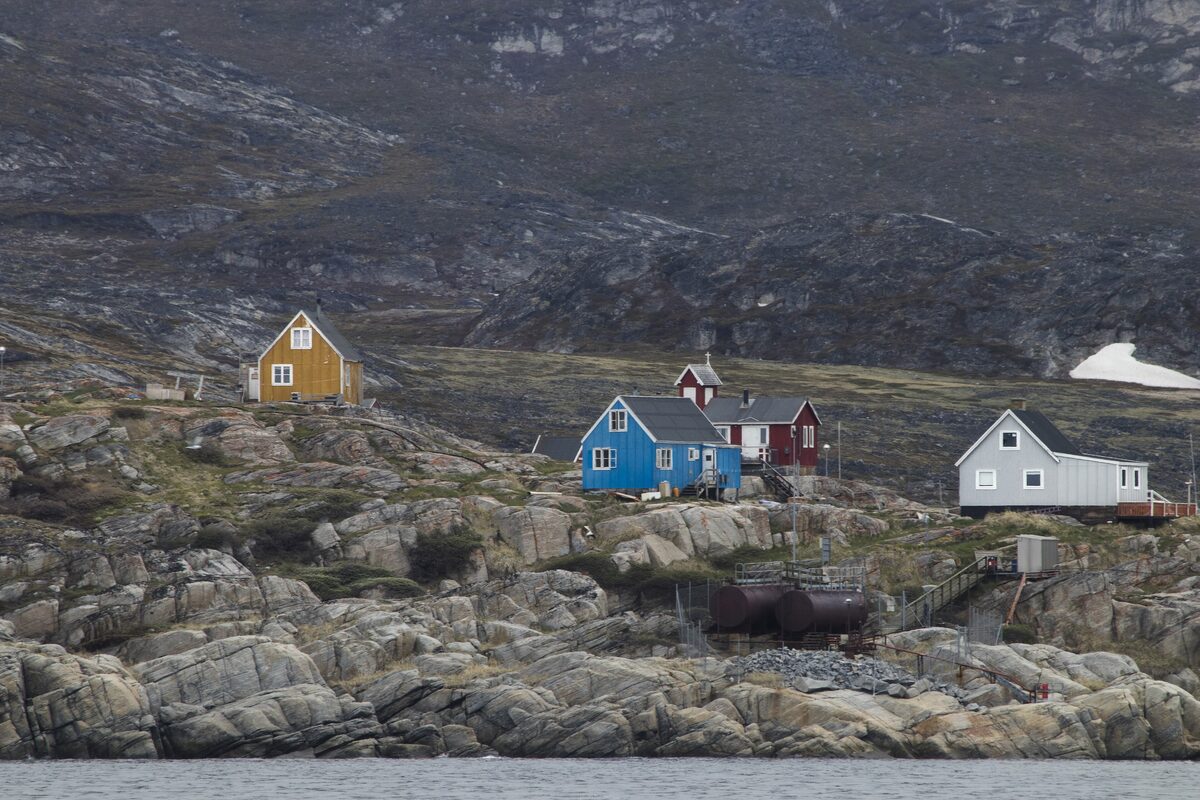 Small colored houses on the rocky shore of Ilimanaq, with grey hills rising behind