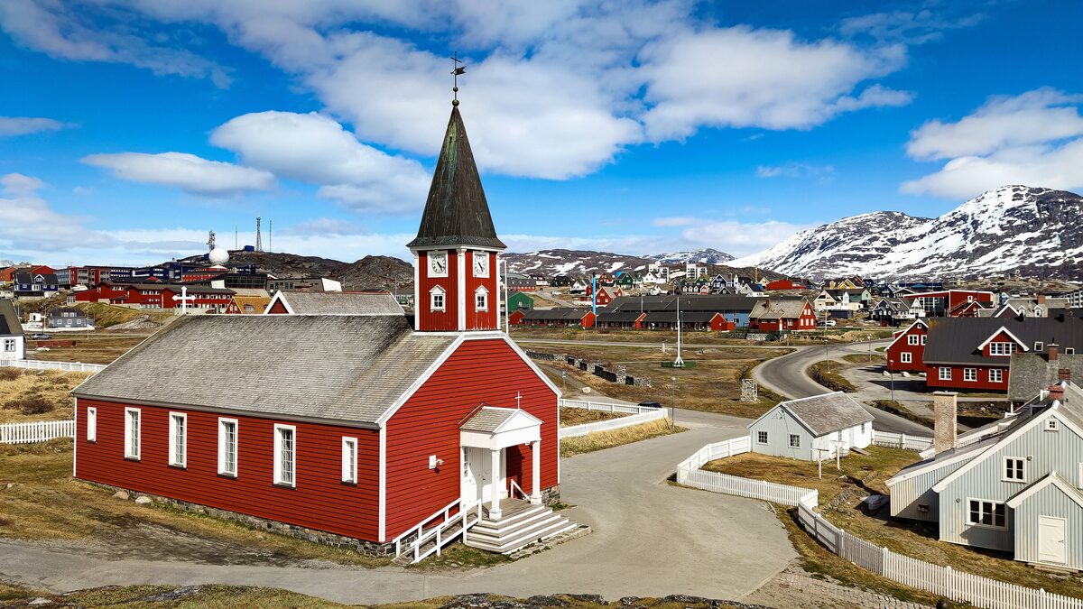 The red wooden church of Nuuk with a tall spire above the town and mountains behind