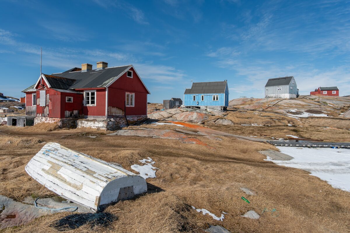 Red and blue houses on the rocky ground at Oqaatsut, with an old white boat lying on the grass