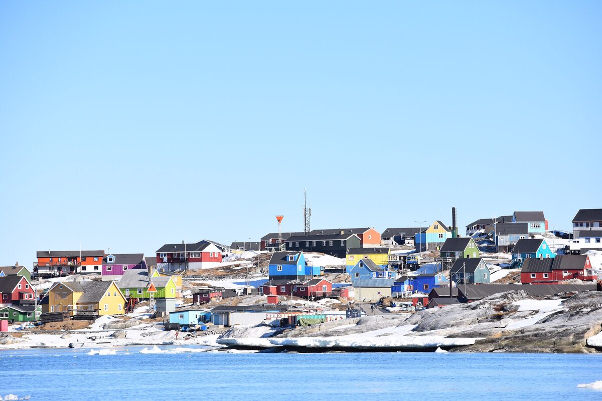 The town of Qeqertarsuaq on Disko Island, colorful houses above a snowy shore and blue water