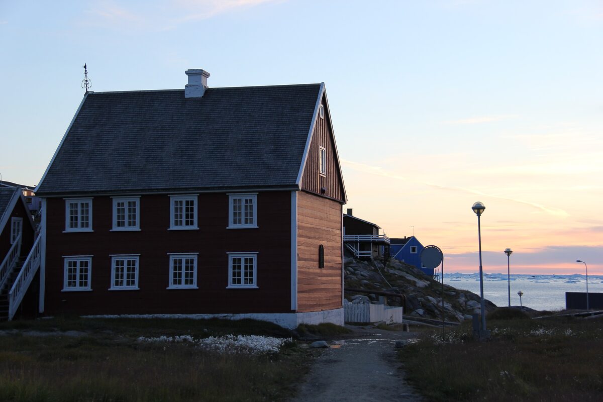 The old vicarage in Ilulissat, a dark red wooden house where Knud Rasmussen was born, at dusk by the bay