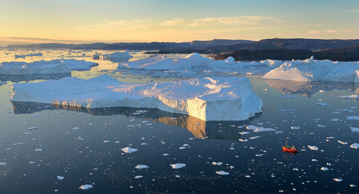 A small red boat among icebergs in Disko Bay, with the low sun lighting the ice