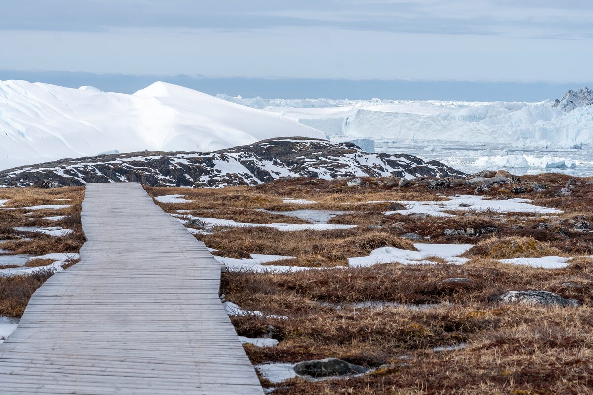 A wooden boardwalk running over brown tundra toward the ice of the Icefjord