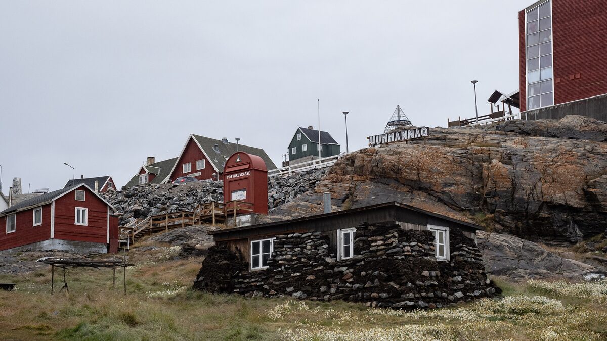 A stone-walled house and red buildings on the rocky hillside of Uummannaq, with a hill behind