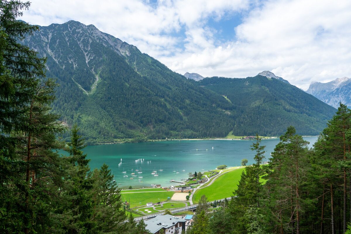 The turquoise Achensee seen through pine trees, between steep green mountains