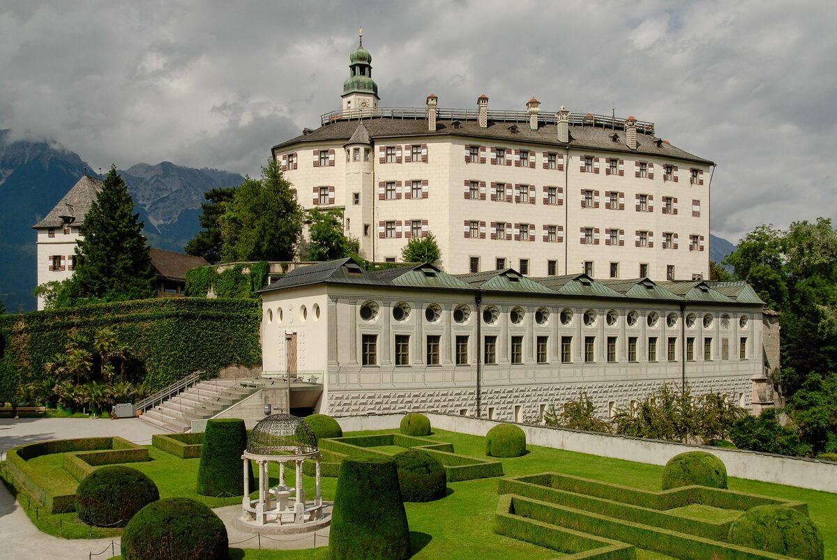 The white upper castle of Ambras above its formal garden, with mountains behind