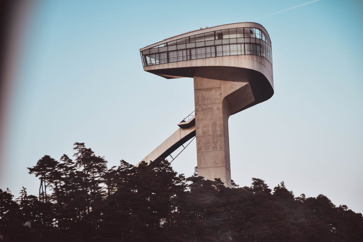 The Bergisel ski jump tower by Zaha Hadid, a slender concrete tower with a curved glass head, above the trees