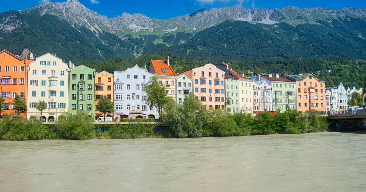 A row of colorful houses on the bank of the Inn in Innsbruck, with the green slopes and rocky peaks of the Nordkette behind