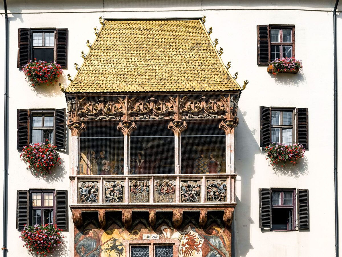 The Golden Roof, a late Gothic balcony with carved reliefs and a roof of gilded copper tiles, between windows with red geraniums