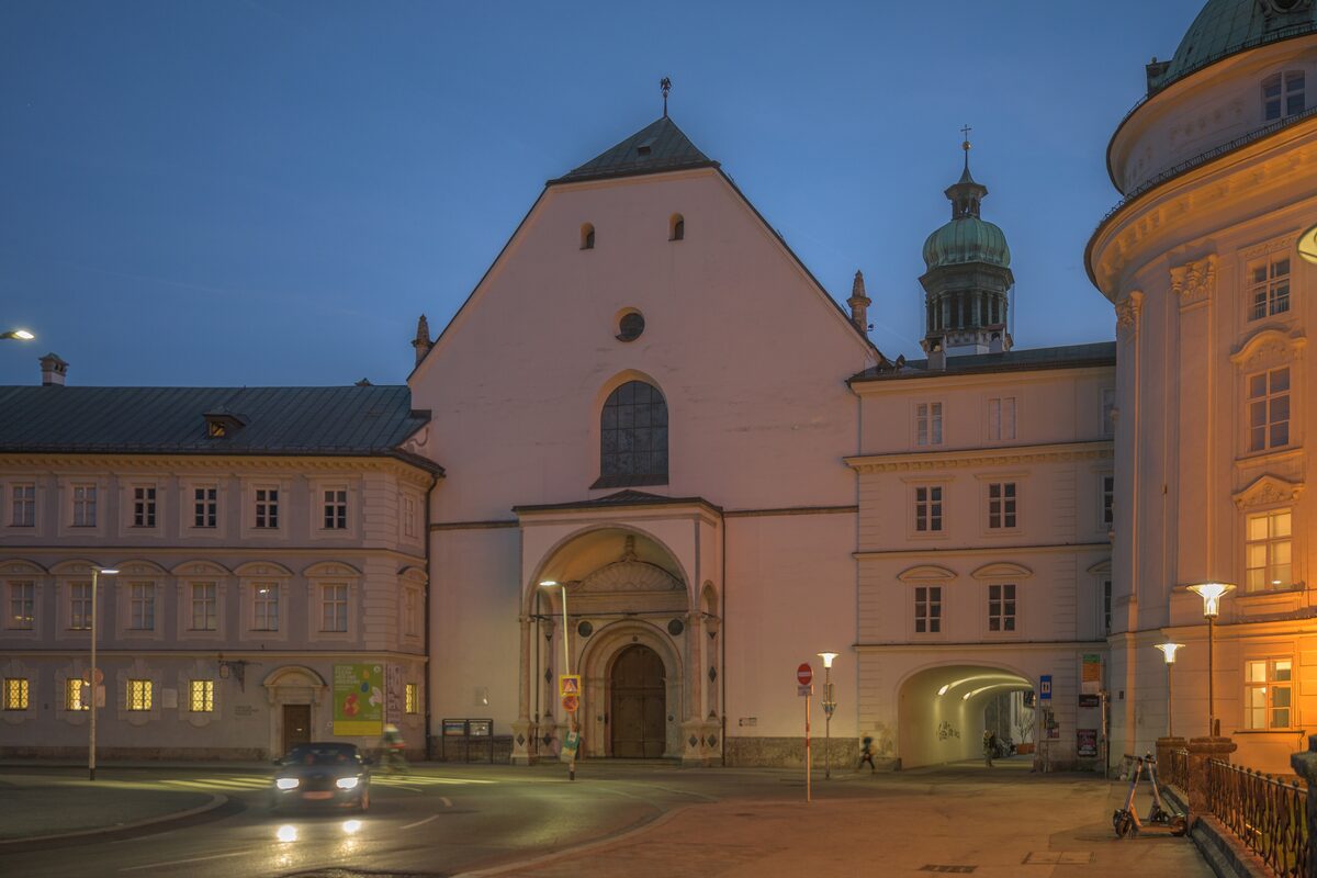 The pale facade of the Hofkirche in Innsbruck at dusk, with the tower of the Hofburg beside it