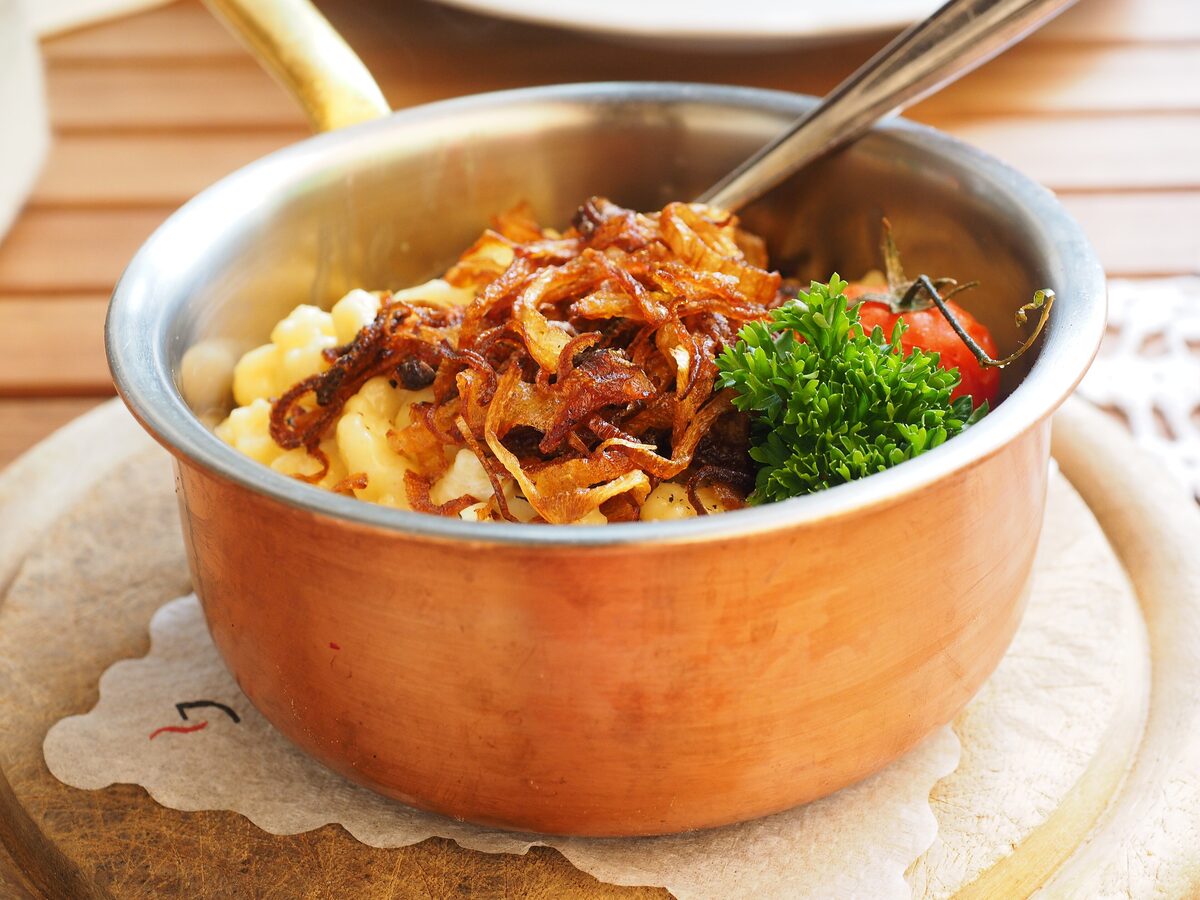 A copper pan of cheese noodles with crispy fried onions