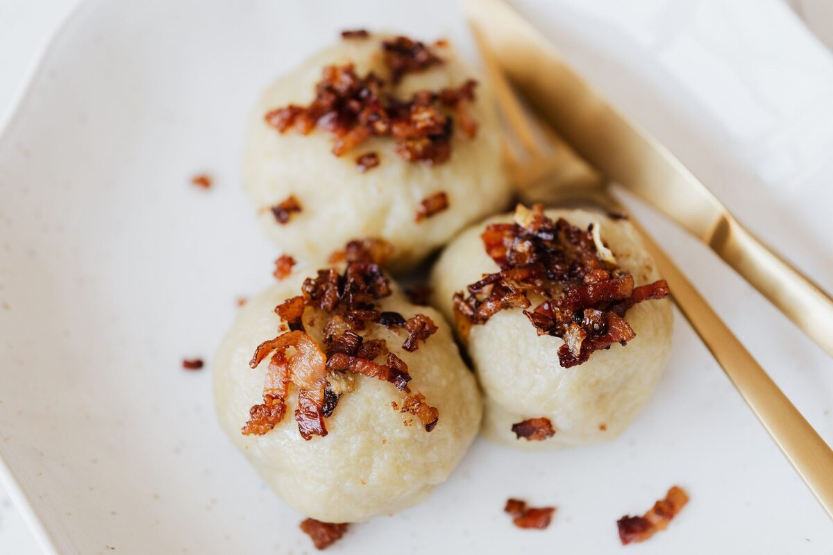 Potato dumplings topped with crispy bacon bits on a ceramic plate