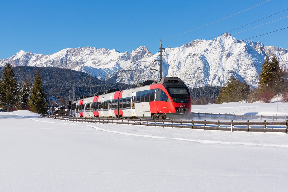 A red and white regional train on the Karwendel railway near Seefeld in the snow, with the Karwendel peaks behind