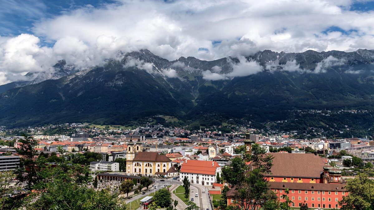 Innsbruck's rooftops and church towers below the wall of the Nordkette mountains, with clouds on the peaks