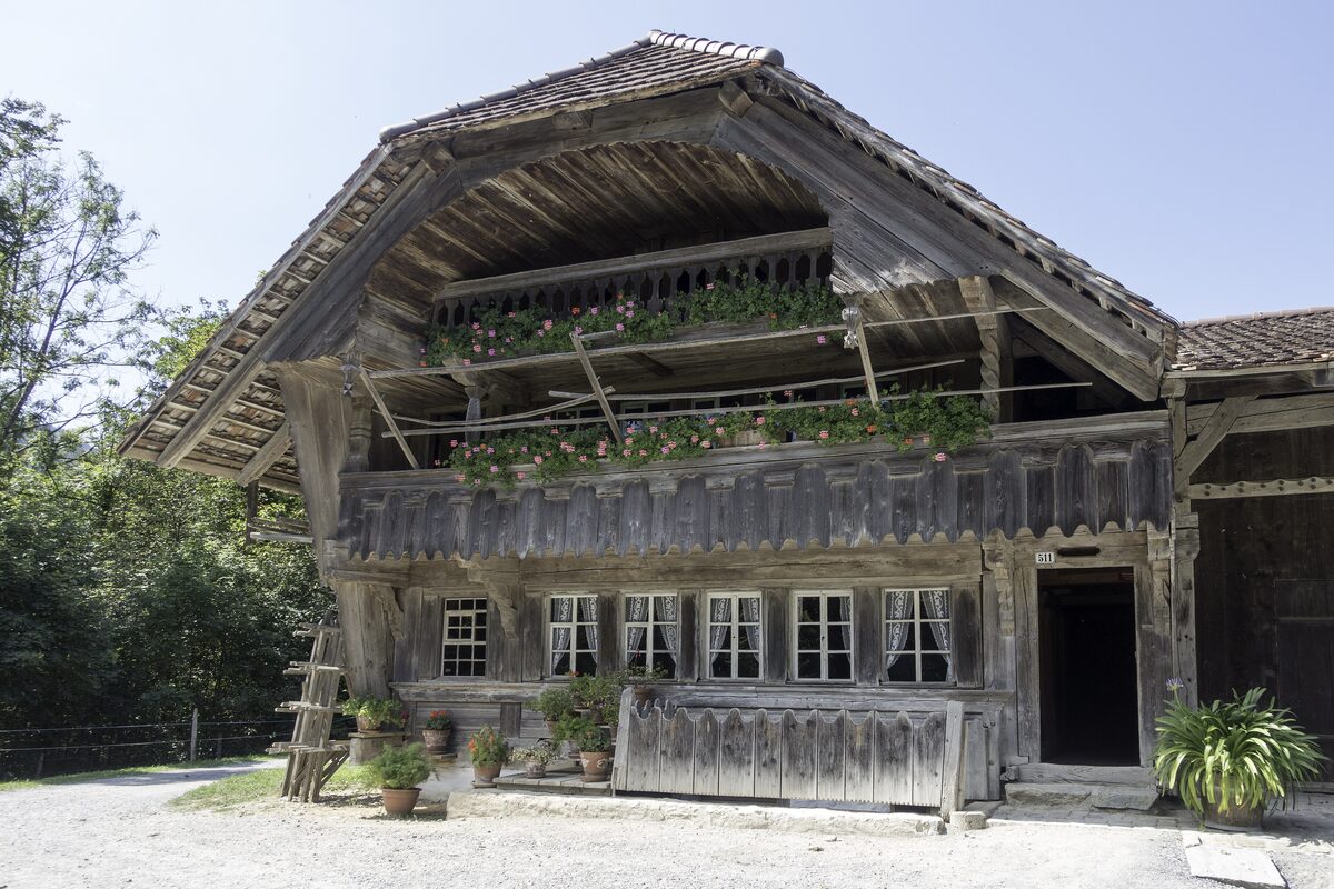 A large weathered Bernese farmhouse with flower boxes along its balconies and a wide overhanging roof at the Ballenberg open-air museum