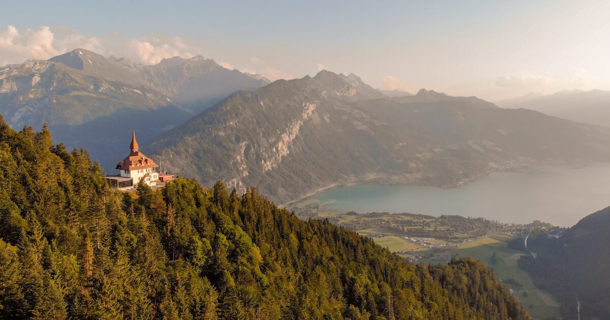 The Harder Kulm restaurant on its forested hill above Lake Thun, with the Bernese Alps in summer haze beyond
