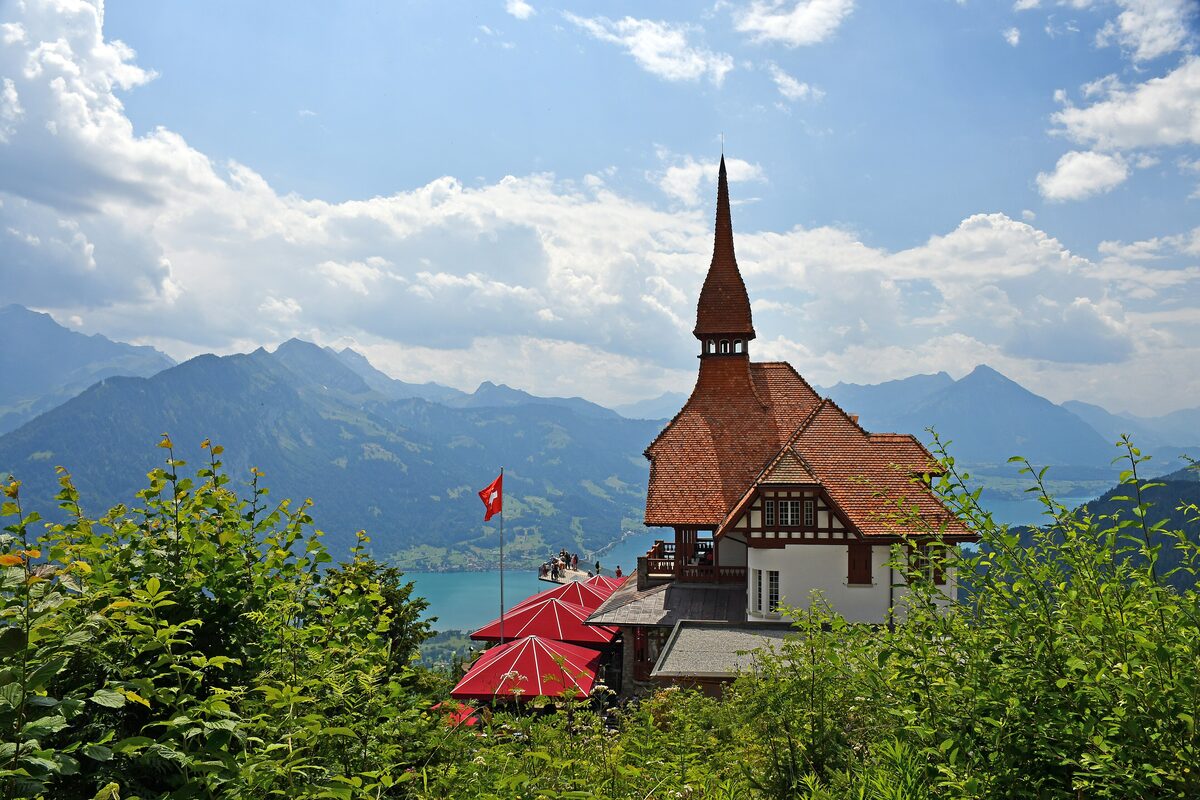 The Harder Kulm restaurant with red umbrellas on its terrace and Lake Thun below in the distance