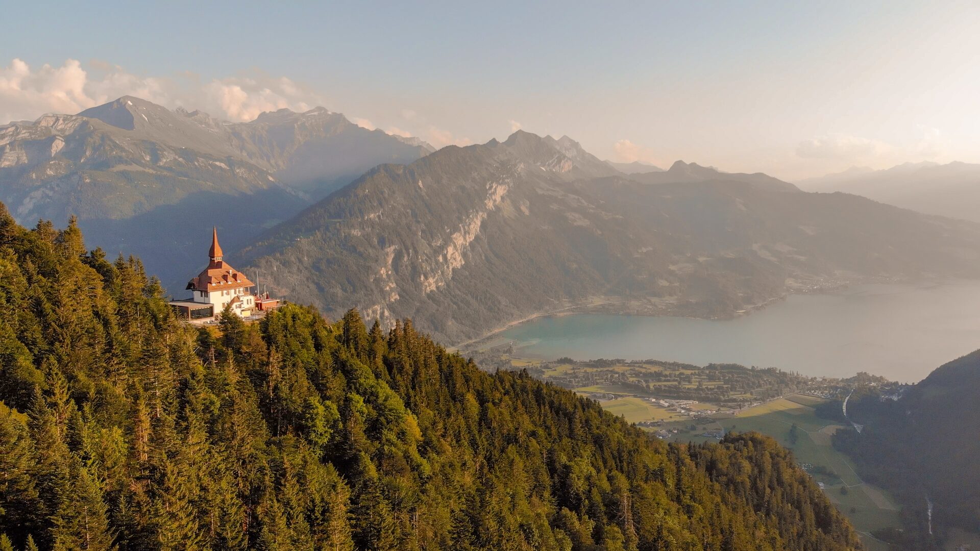 The Harder Kulm restaurant on its forested hill above Lake Thun, with the Bernese Alps in summer haze beyond