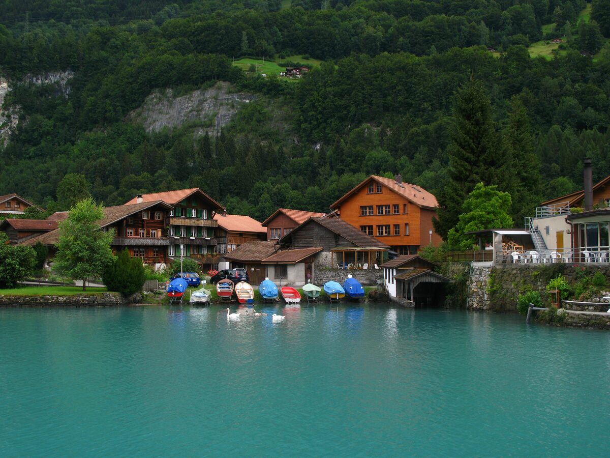 Colorful rowboats at the shore in Iseltwald, with village houses and a forested slope above Lake Brienz