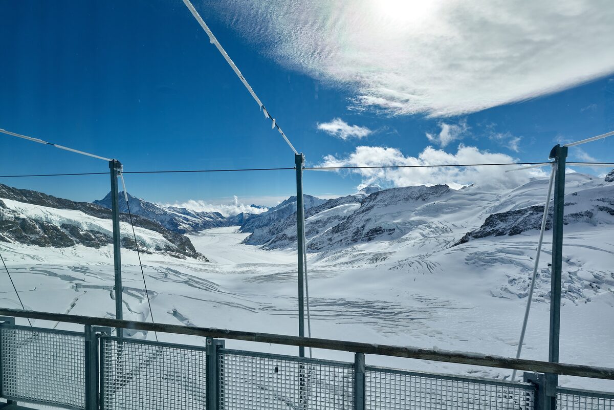 The Aletsch Glacier, a wide river of ice and snow, seen from the Sphinx viewing terrace at the Jungfraujoch through its railings and wires