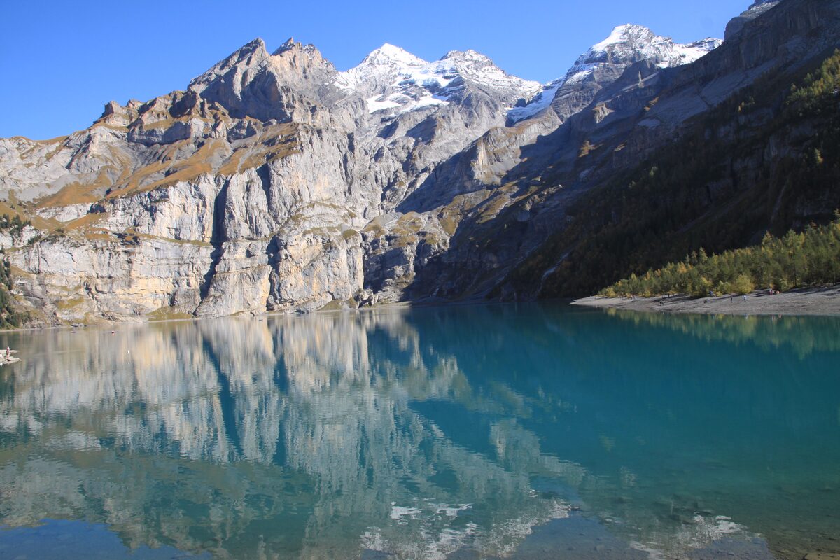Turquoise Lake Oeschinen mirroring the steep limestone walls and snow-capped peaks of the Blüemlisalp above it