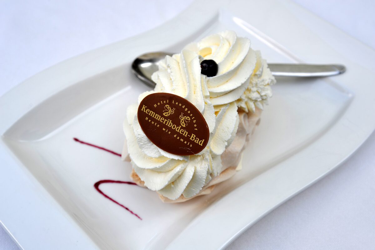 A meringue topped with swirls of whipped cream and a chocolate disc on a white plate