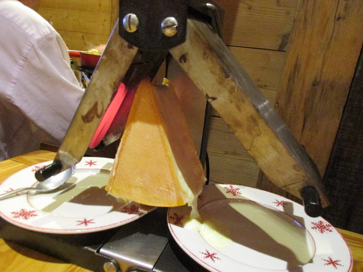 Half a raclette cheese in a table heater, with melted cheese dripping onto a plate in a wood-paneled room