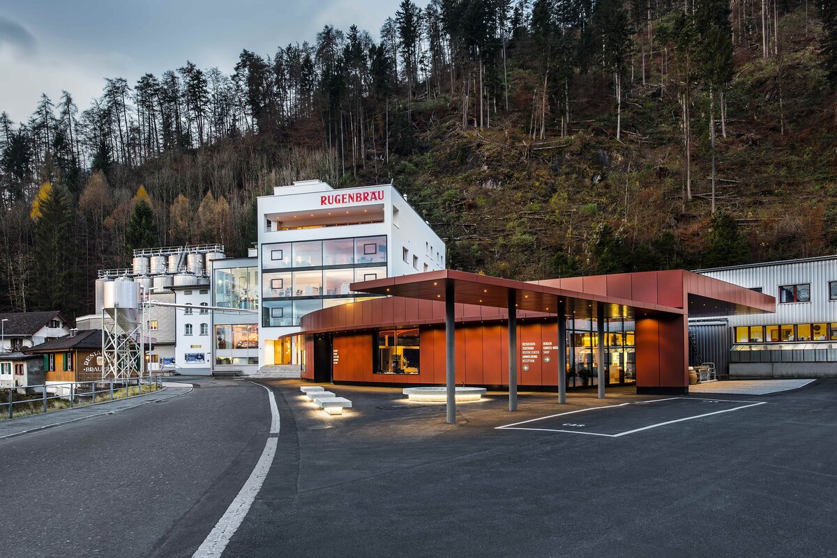 The Rugenbräu brewery in Interlaken at dusk, a white building with its name on the facade and silos behind the red visitor center