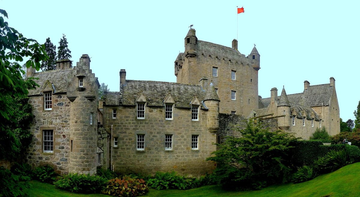 Cawdor Castle, a gray stone tower house with turrets and a flag, behind green gardens