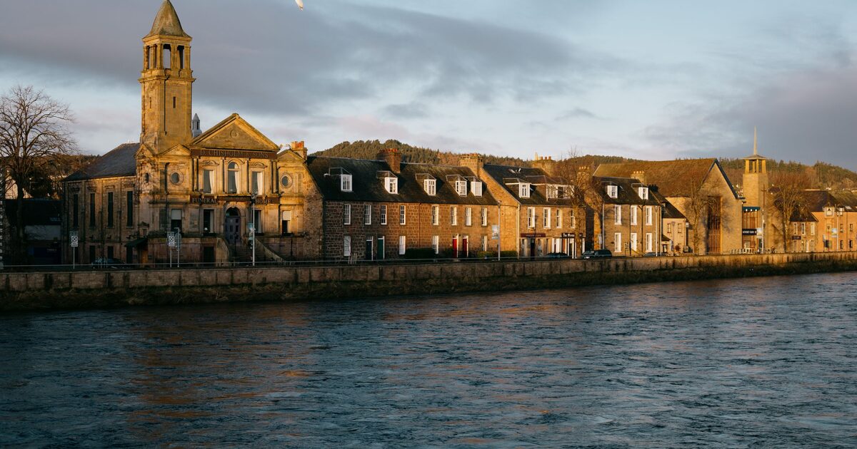The River Ness in Inverness at sunrise, with a church tower and a row of old stone houses along the far bank