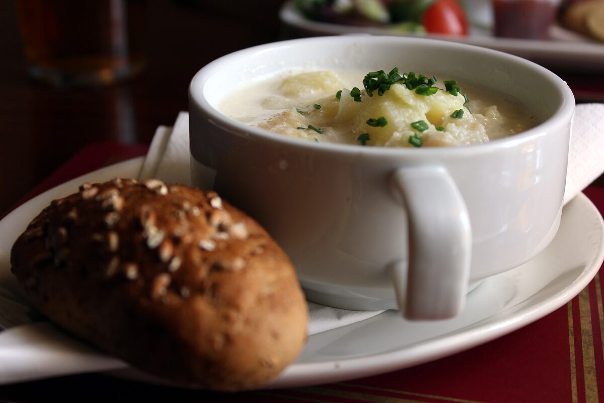 A cup of Cullen skink soup with smoked haddock and potato, with a brown bread roll