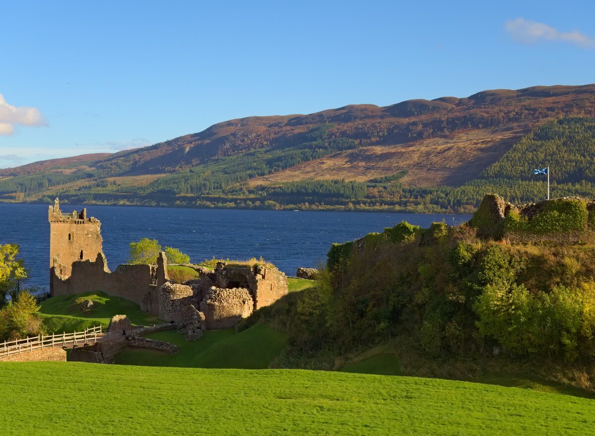 The ruined tower of Urquhart Castle on a green promontory above Loch Ness, with hills on the far shore in autumn colors