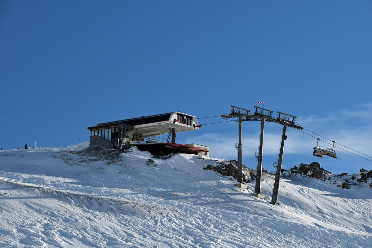 The Idjochbahn top station under a blue sky, with the lift cable and snow around it
