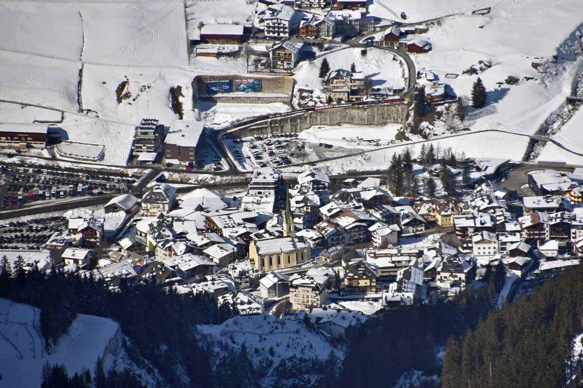 Ischgl seen from above in winter, with snow-covered roofs around the church and a road curving up the slope