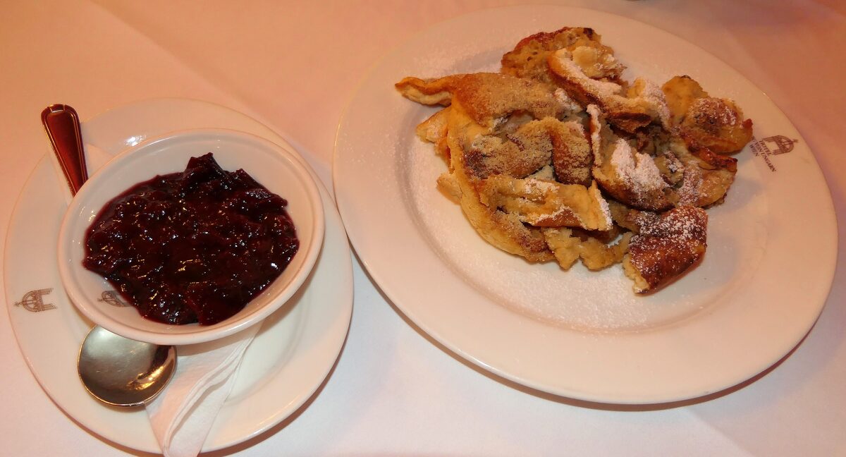 A plate of torn pancake pieces next to a small bowl of dark fruit compote on a table