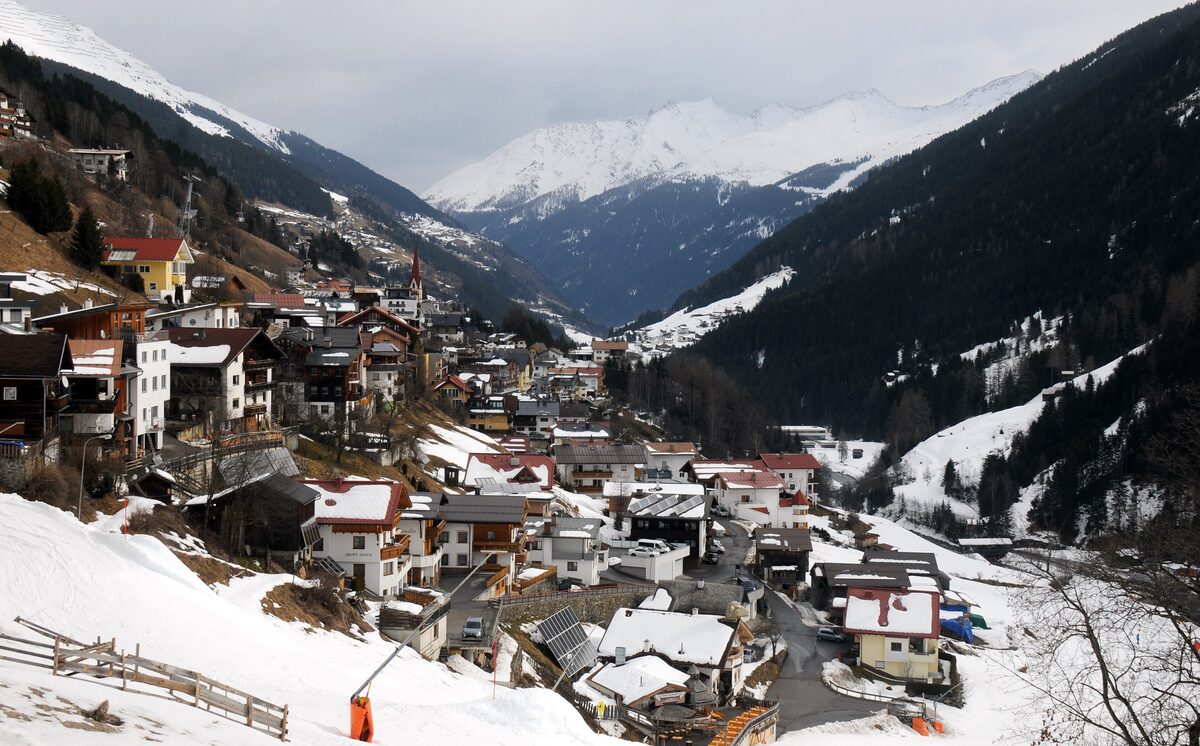 The village of Kappl in a snowy valley, with a snowy slope in the foreground and mountains behind