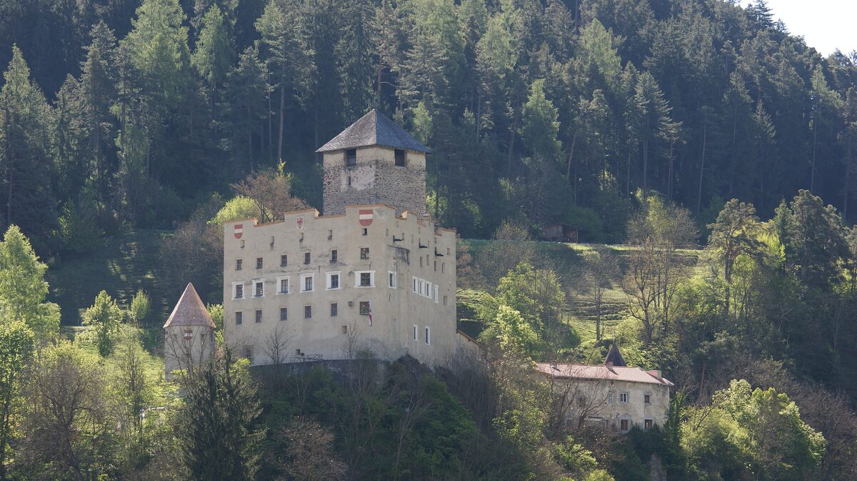 Schloss Landeck, a pale stone castle with a square tower on a wooded slope above the town