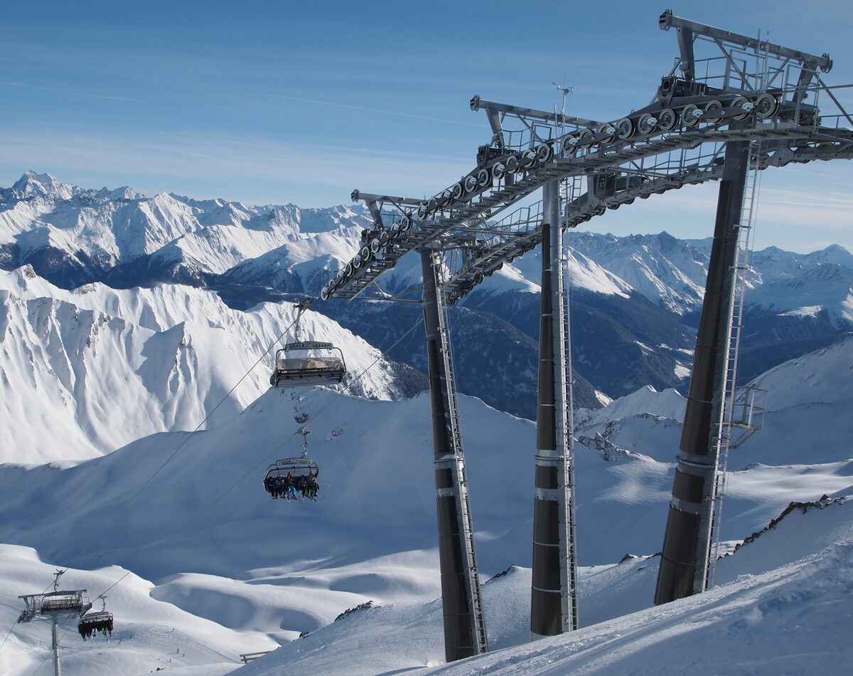 A chairlift passing a lift pylon above snowy mountains and ridges on a clear day