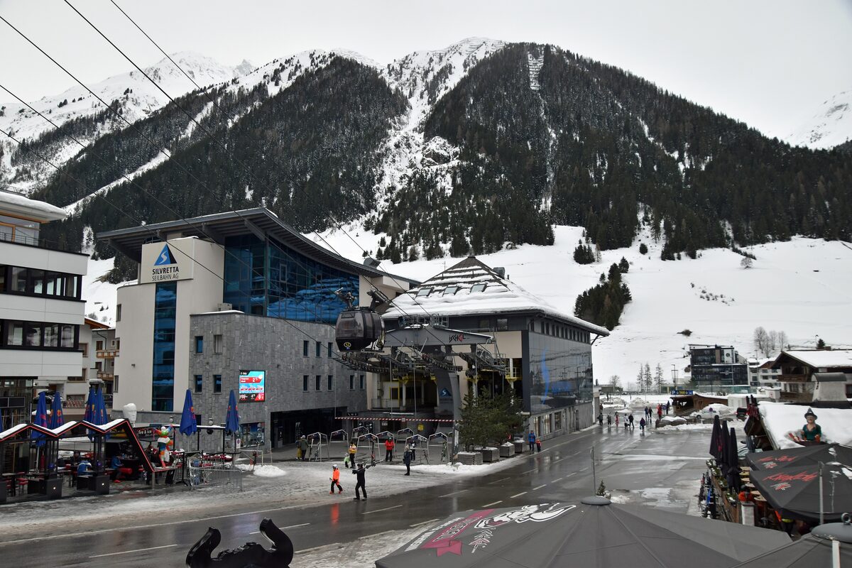The Silvretta Seilbahn building on Ischgl's main street, with a gondola cabin above the road and a wooded, snowy mountain behind