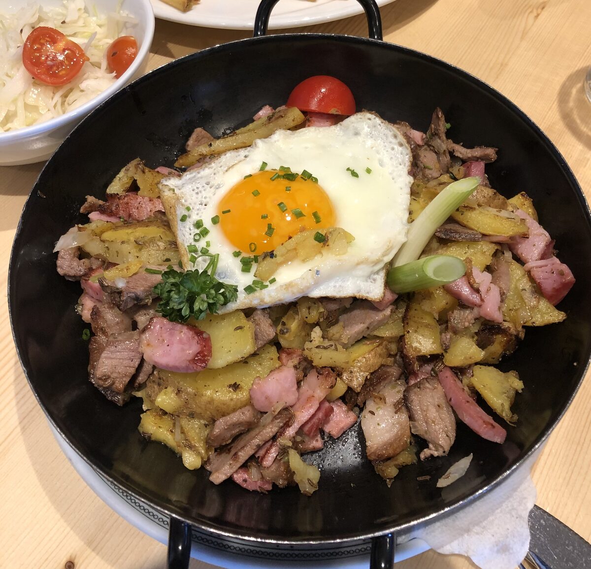 A pan of fried potatoes with meat and bacon, topped with a fried egg