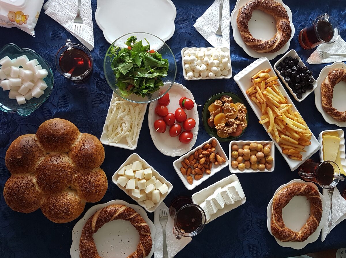 Overhead view of a Turkish breakfast spread with simit, cheeses, olives, tomatoes, honey, dried fruit and glasses of tea