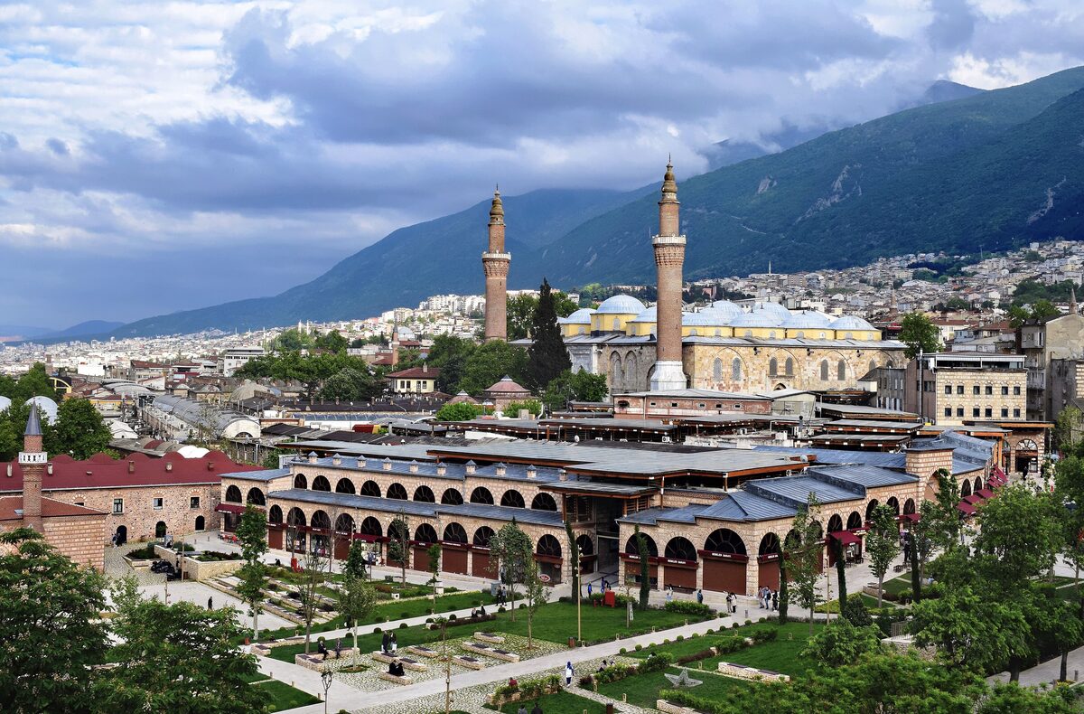 Bursa's Grand Mosque with its two minarets and many domes above the arcaded Koza Han, with Mount Uludağ behind