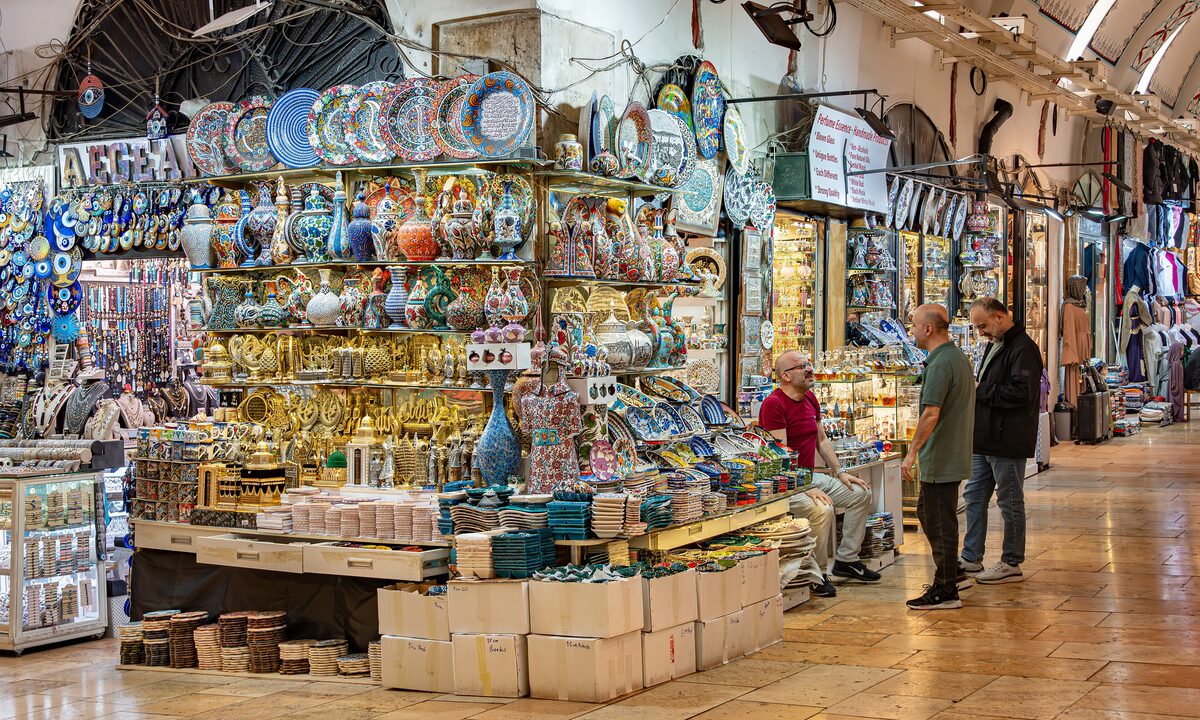 A Grand Bazaar shop piled with painted ceramic plates, bowls and lamps, with shoppers in the vaulted lane