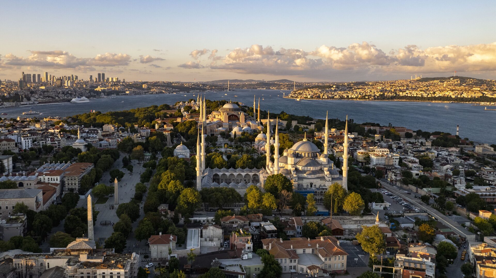 Aerial view of Sultanahmet at golden hour, with the Blue Mosque and its six minarets in front, Hagia Sophia behind it and the Bosphorus and the Asian shore beyond