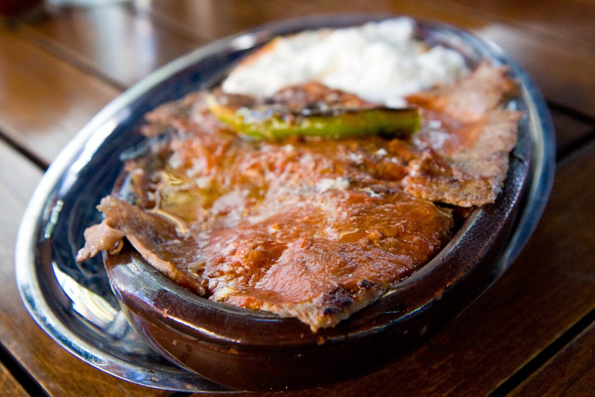 İskender kebab of sliced döner meat on bread with tomato sauce, yogurt and a green pepper, in a copper dish