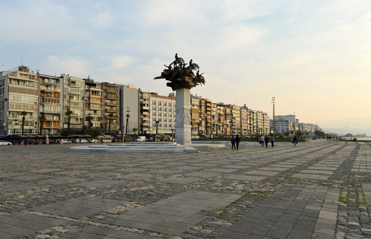Gündoğdu Square on the Alsancak waterfront, a wide paved square with a bronze monument in the middle and apartment blocks behind it