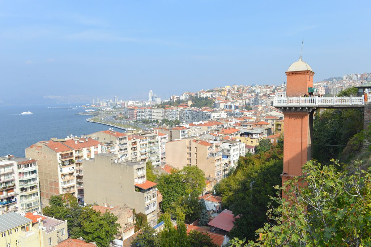The red brick tower of the Asansör rising above the rooftops of Karataş, with the gulf and the waterfront apartments of İzmir behind it