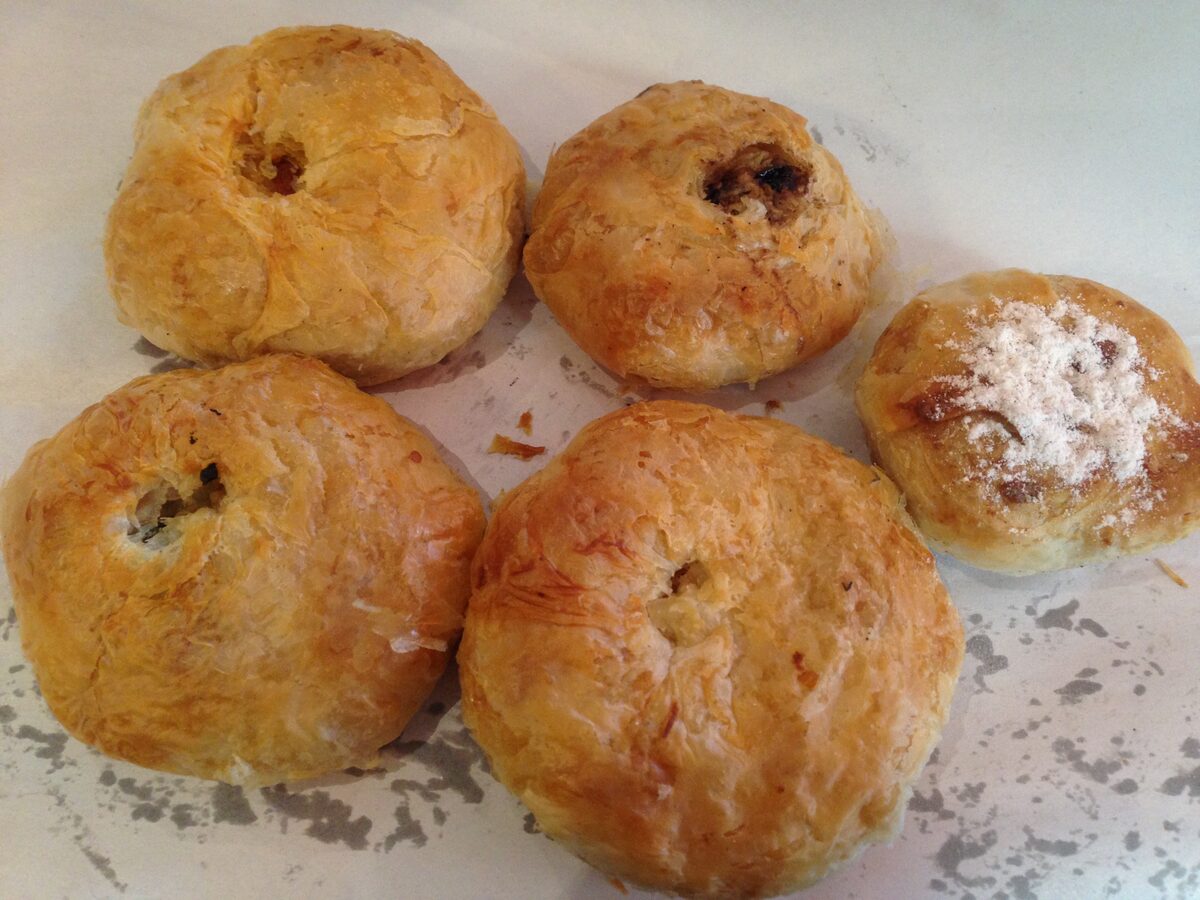 Five golden, flaky boyoz pastries on a paper-covered tray