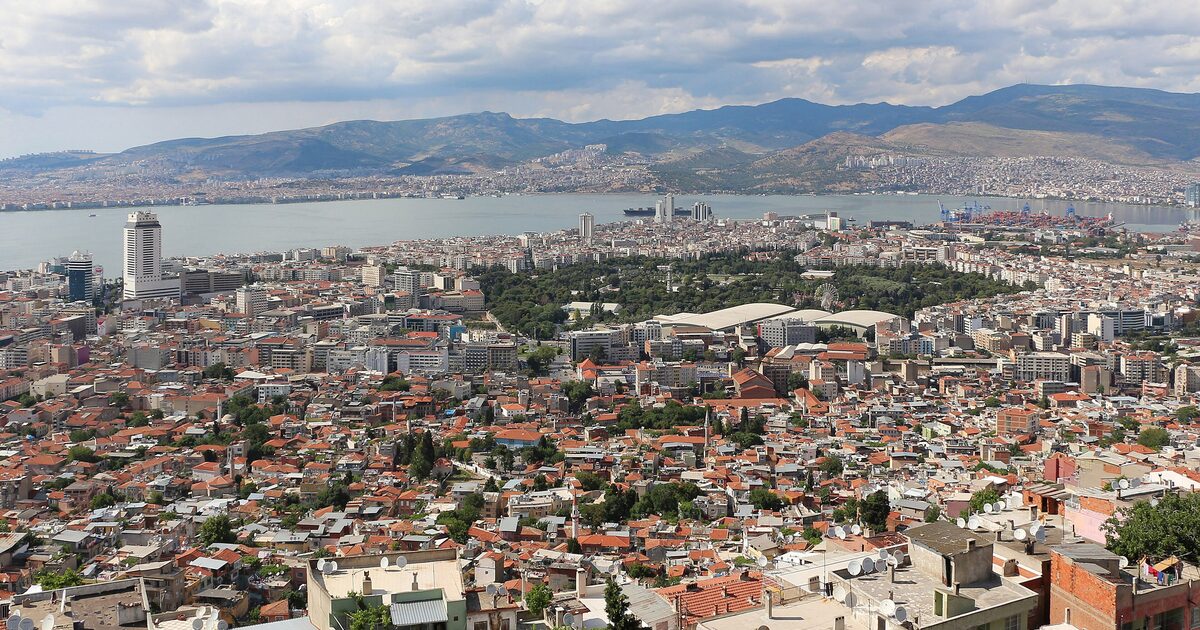İzmir seen from Kadifekale hill: red-roofed houses running down to the green of Kültürpark, the gulf behind them and Karşıyaka and the mountains on the far shore
